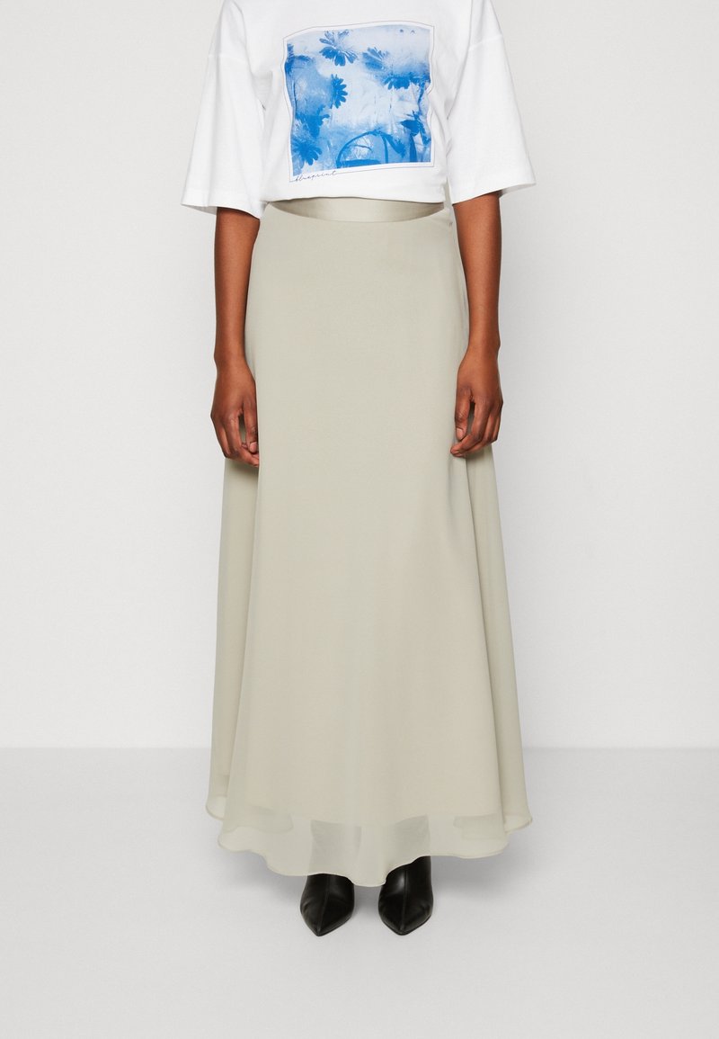 Lång, flödande ljusbeige kjol i mjukt tyg, tillsammans med en vit t-shirt med grafiskt tryck som har blå blommönster. Svarta klackstövlar.