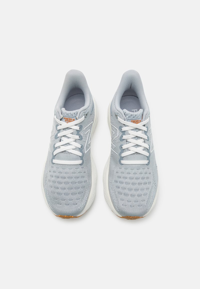Een paar lichtgrijze gebreide hardloopschoenen met witte zolen en veters, van bovenaf getoond op een witte achtergrond.