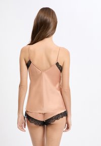 Satynowa koszulka na ramiączkach w delikatnym odcieniu brzoskwini z regulowanymi paskami, zestawiona z dopasowanymi szortami zdobionymi czarną koronką na krawędziach.