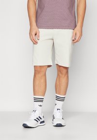 Ljust färgade shorts i avslappnad passform, i kombination med ett mönstrat rödvitt skärp, vita skor och svartspräckliga strumpor.