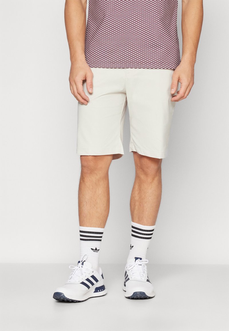 Ljust färgade shorts i avslappnad passform, i kombination med ett mönstrat rödvitt skärp, vita skor och svartspräckliga strumpor.