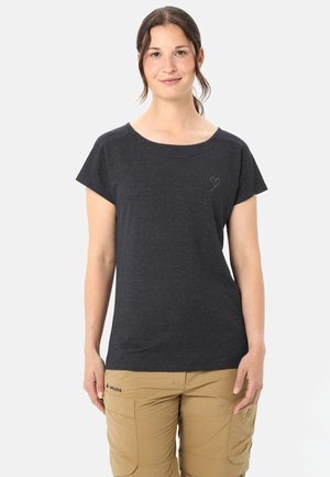 Donna con capelli scuri raccolti in una coda di cavallo che indossa una maglietta a maniche corte grigio scuro con un piccolo disegno a forma di cuore e pantaloncini cargo marrone chiaro.