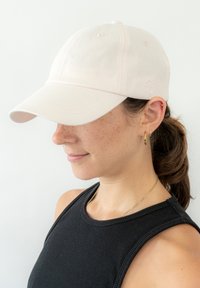 Gorra de béisbol de color rosa claro en tela de algodón con visera curvada, que presenta un detalle de logotipo bordado y seis ojales de ventilación en la parte superior.