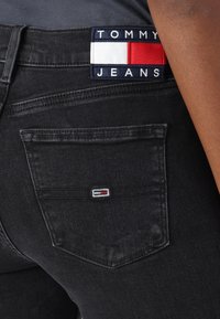 Fekete farmernadrág hátsó zsebbel, amelyen egy kis hímzett logó található piros, fehér és kék színekben. Márkanevével ellátott címke a derékpánton.