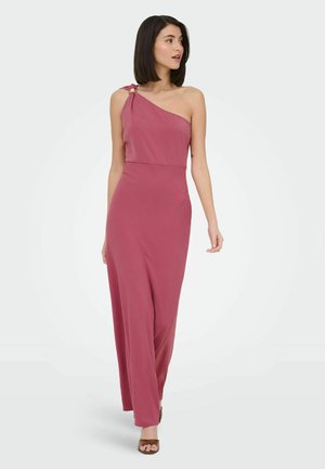 Kvinde med skulderlangt mørkt hår iført en lang, enkelt skulder mauve kjole og brune åbne tå-hæle, der kigger mod sin venstre side.