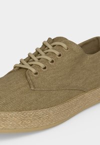 Μπεζ καθημερινό παπούτσι με κορδόνια και υφασμάτινο επάνω μέρος, υφασμένη υφή στη σόλα, πλάγια γωνιακή άποψη σε ανοιχτό φόντο.