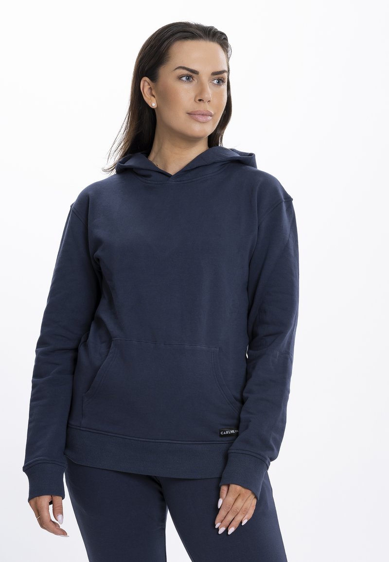 Hanorac bleumarin dintr-un material moale, având buzunar tip kangur, manșete și tiv cu pliuri, cu un etichetă logo în partea stângă jos.