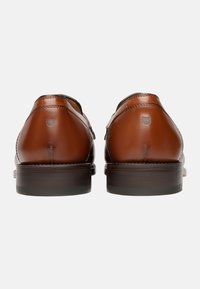 Scarpe da uomo in pelle marrone con finitura liscia, dettagli cuciti e tacco quadrato. Le suole sono scure e con texture.