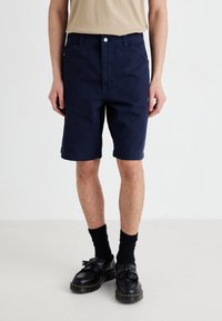 Navy blue cotton shorts with a standard fit, featuring side pockets and a folded hem. Worn with black shoes and knee-high socks.