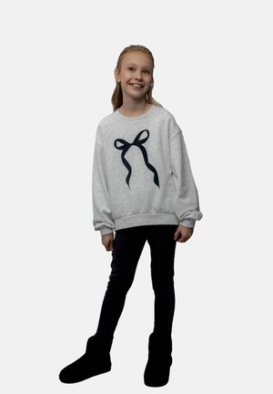 Szary sweter z czarną grafiką wstążki z przodu, w zestawieniu z czarnymi legginsami i botkami za kostkę. Miękka tkanina i luźny krój.