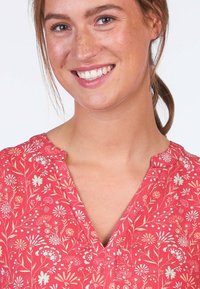 Rote Bluse mit V-Ausschnitt und weißen sowie pastellfarbenen Blumenmustern. Leichtes Material mit einem lockeren Schnitt.