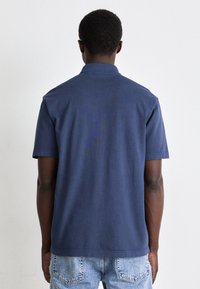 Mörkblå polo med klassisk krage och korta ärmar, tillverkad av bomull, med rak fåll och subtil textur.