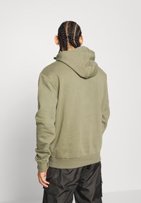 Haut à capuche vert olive au design ajusté, avec des poignets et un ourlet côtelés, et une capuche. Texture lisse sans motifs ni accents visibles.