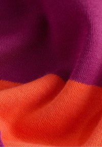 Tissu tricoté violet et orange avec une texture visible et des plis doux créant un motif ondulé.