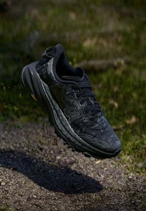 Black running shoe with a textured upper, featuring a mesh tongue, rubber outsole, and patterned detailing. Lightly lifted above ground.