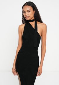 Μαύρο ριπ πλεκτό φόρεμα με σχέδιο halter neck, που διαθέτει πλάγιο σκίσιμο και μία μακριά κορδέλα δέσιμο. Λείο υλικό, εφαρμοστή σιλουέτα.