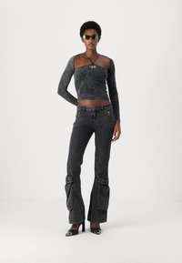 Crop top noir à manches longues avec une finition texturée et un logo central, associé à un jean noir à jambes larges avec des poches décoratives.