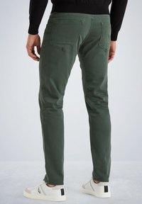 Pantalones de algodón verdes con corte ajustado, que cuentan con bolsillos traseros, una pretina y se combinan con zapatillas blancas. Textura suave, diseñados para la comodidad.