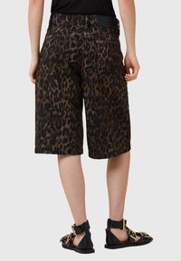 Shorts en denim à imprimé léopard avec une coupe décontractée, dotés d'une taille mi-haute et de poches arrière, associés à des sandales noires et à des accessoires en or.
