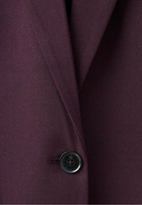 Tissu bordeaux à texture lisse avec un détail de bouton noir. Comprend un col à revers cranté et une coupe ajustée.