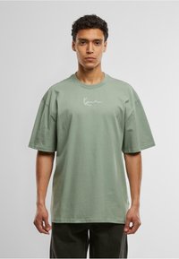 Light green oversized t-shirt made of cotton, featuring a round neckline and short sleeves, with a white signature graphic on the chest.