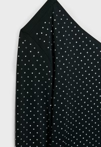 Crni fabrici top s asimetričnim dekolteom, ukrašen brojnim malim, okruglim srebrnim zakovicama ravnomjerno raspoređenim po površini.