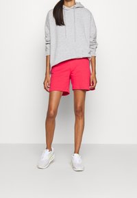 Šedá mikina s kapucí, růžové kraťasy a bílé tenisky s pastelovými akcenty. Kraťasy mají elastický pas a sahají až ke kolenům.