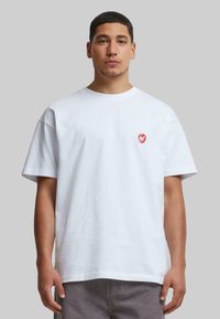 Hvid bomulds t-shirt med korte ærmer, der har et rødt hjerte-logo på venstre bryst. Enkel, afslappet pasform med rund hals.
