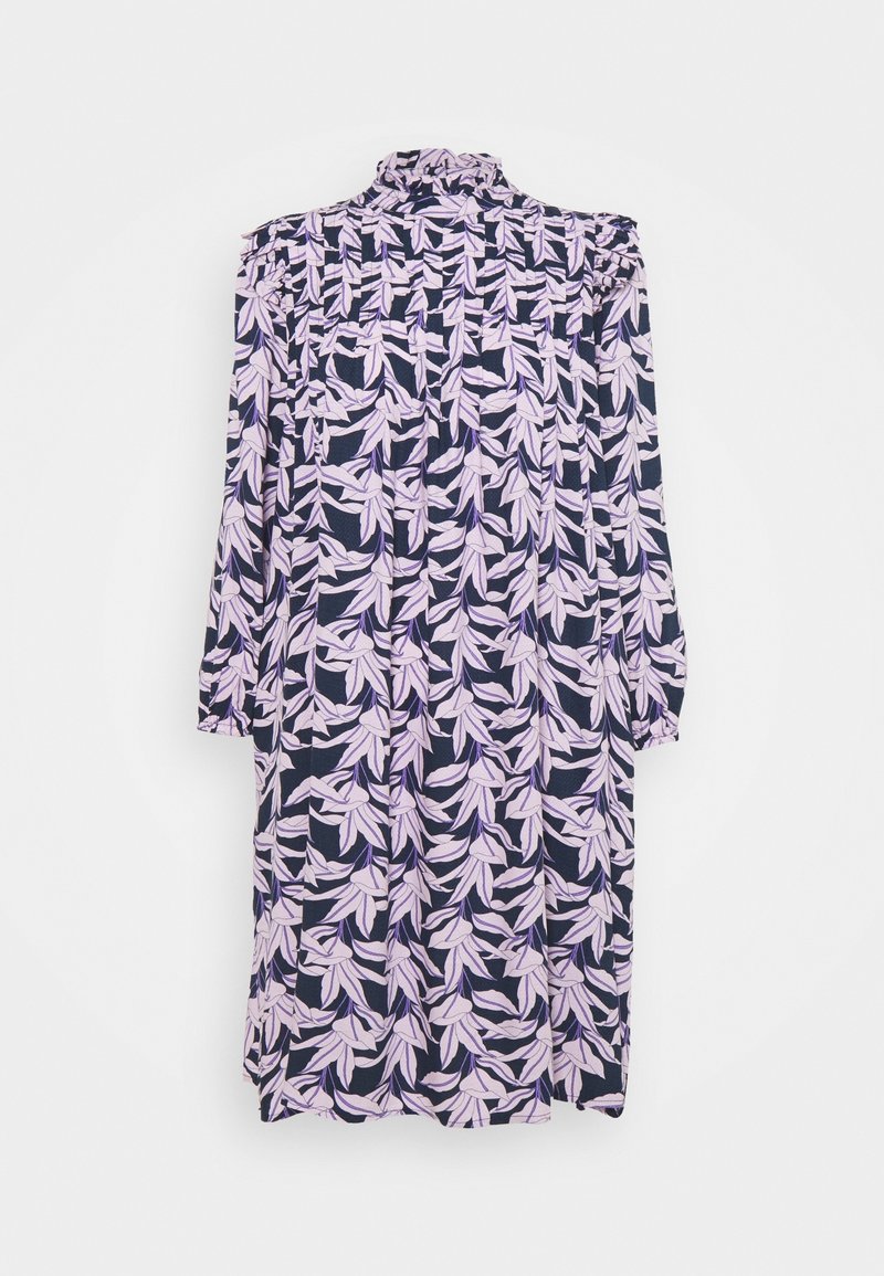 Robe à manches longues avec col montant et motif de feuilles roses sur fond sombre, suspendue contre un mur blanc uni.