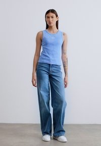 Ανοιχτό μπλε αμάνικο τοπ με στρογγυλή λαιμόκοψη, συνδυασμένο με φαρδιά ξεβαμμένα μπλε τζιν παντελόνια και λευκά αθλητικά παπούτσια. Απλό και καθημερινό σύνολο.