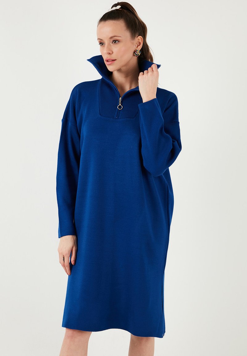 Rochie sweat din bumbac, supradimensionată, de culoare albastră, cu guler înalt și fermoar pe jumătate. Se remarcă prin detalii ribe pentru guler și slituri laterale la tiv.