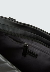 Interieur van een zwarte leren handtas met een ritszak, een gladde voering en een label. Het ontwerp is gestructureerd met een gepolijste afwerking.