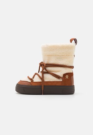 Brown and cream winter boot with a plush fabric upper, suede accents, a sturdy rubber sole, and dark brown laces for adjustment.