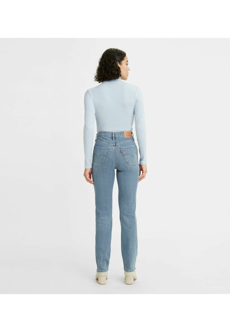 Parte superior de manga larga azul combinada con pantalones vaqueros de mezclilla azul claros con corte recto y un parche de cuero marrón con el logo en la parte trasera de la cinturilla.