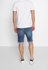 Džínové šortky ve středně modré barvě s ohrnutými konci, rovný střih a zadní kapsy. Spárované s hladkým bílým tričkem s krátkým rukávem a bílými botami.