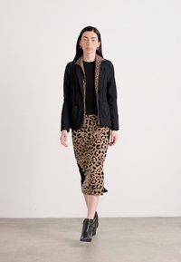 Giacca nera con fodera in stampa leopardata, top nero e gonna a tubino beige con stampa leopardata. Stivali neri alla caviglia. Tessuti morbidi e forme aderenti.