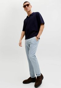 Μπλούζα πόλο με κοντά μανίκια σε ναυτικό μπλε, ανοιχτόχρωμο μπλε παντελόνι, καφέ σαουέτ μοκασίνια και κομψά καφέ γυαλιά ηλίου. Απλός, μοντέρνος σχεδιασμός, άνετη γραμμή.