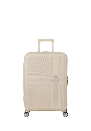 Valigia rigida beige con motivi a cerchi concentrici, manico telescopico, quattro ruote girevoli e emblema del marchio circolare sulla parte anteriore.