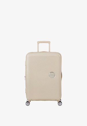 Valigia rigida beige con motivi a cerchi concentrici, manico telescopico, quattro ruote girevoli e emblema del marchio circolare sulla parte anteriore.