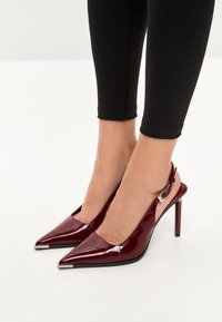 Burgundy patent leather slingback heels with pointed toes, a sleek design, and metallic accents on the toe caps.