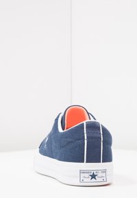 Námořnické plátěné tenisky s bílou podrážkou, červeným vnitřkem, bílými akcenty a nášivkou loga Converse na patě.