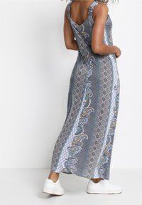 Maxi šaty v modré a bílé barvě s paisley a geometrickými vzory. Mají řasené ramínka a volný střih. Noseny s bílými platformami.