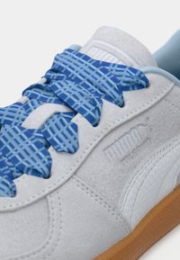 Zapatillas de ante gris con cordones de cuadros azules, que cuentan con una suela de goma y un logo grabado en el lateral. Detalles en azul claro cerca de la lengüeta.