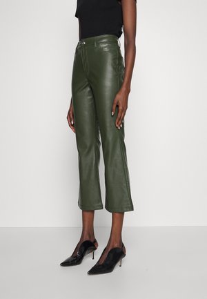 Woman wearing high-waist olive green cropped leather pants paired with black pointed-toe heeled shoes and a black sleeveless top.