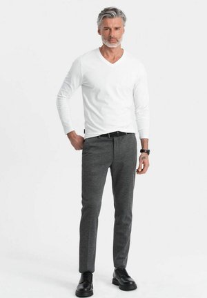 Weißes Langarm-V-Ausschnitt-Shirt, kombiniert mit schmal geschnittenen, dunkelgrauen Hosen und schwarzen Schuhen, die eine subtile Textur und ein elegantes Design aufweisen.