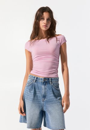 Pink fitted short-sleeve top with a gathered texture, paired with medium-wash denim shorts featuring a high waist and frayed hem.