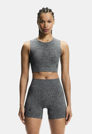 Frau mit geflochtenem Haar, die ein passendes graues, ärmelloses, bauchfreies Oberteil und hoch taillierte Biker-Shorts vor weißem Hintergrund trägt.