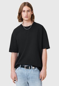 T-shirt nera oversize in cotone con maniche corte, scollatura rotonda e una superficie liscia, abbinata a jeans chiari strappati.