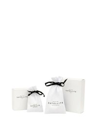 Des boîtes cadeaux blanches et des pochettes en tissu avec des liens noirs, arborant un texte noir indiquant "SATELLITE" et "DEPUIS 1987," mettent en avant un design minimaliste.