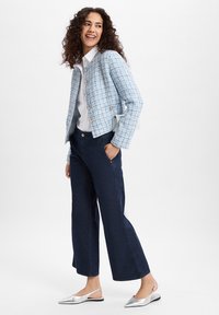 Lichtblauwe tweedjasje met ronde knopen, witte blouse, donkere wijde broek en zilveren slingback flats. Glad textuur en op maat gemaakte pasvorm.